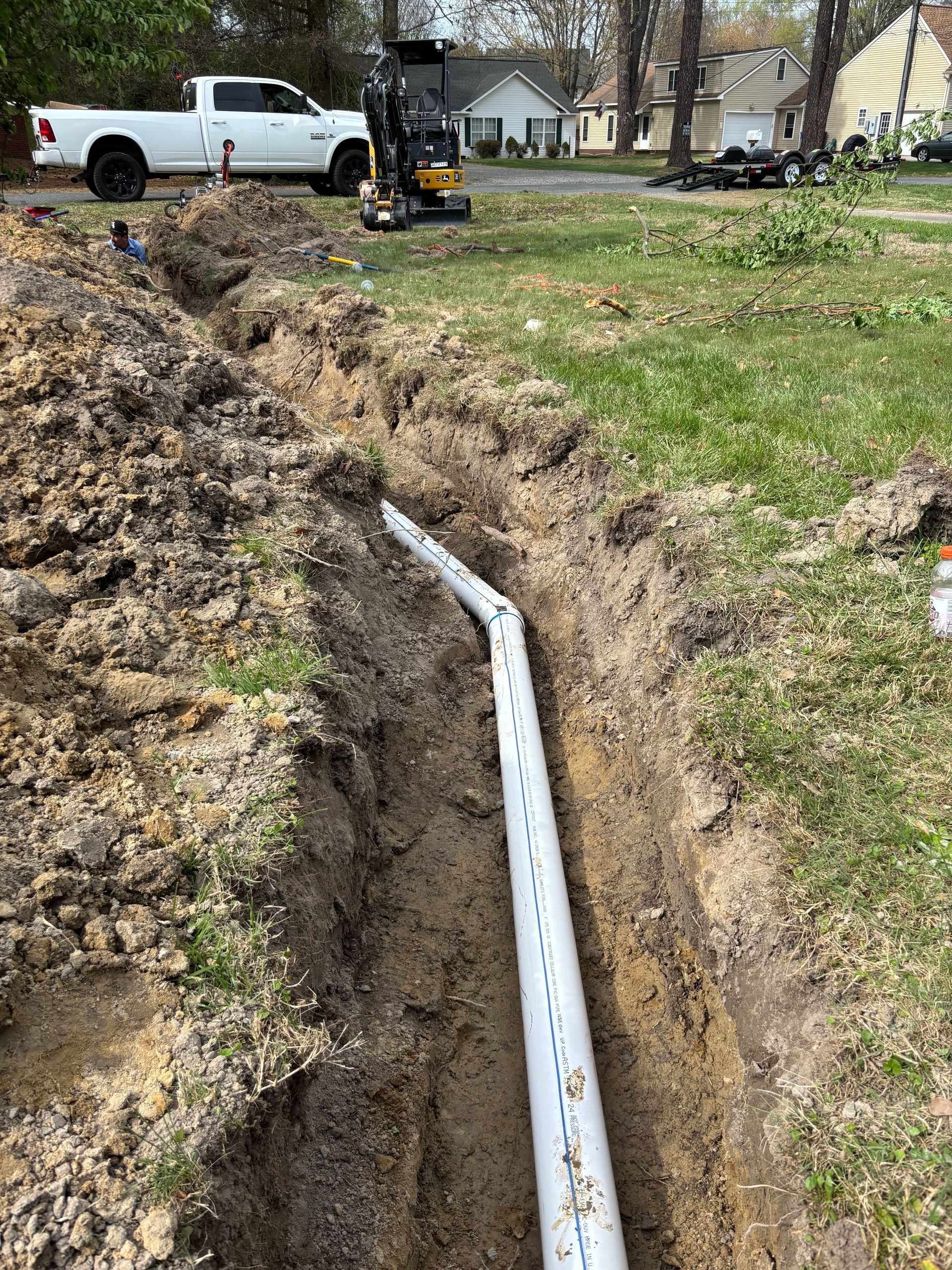 Trench dug in a yard with white PVC pipe installed, near a white pickup truck and residential homes.