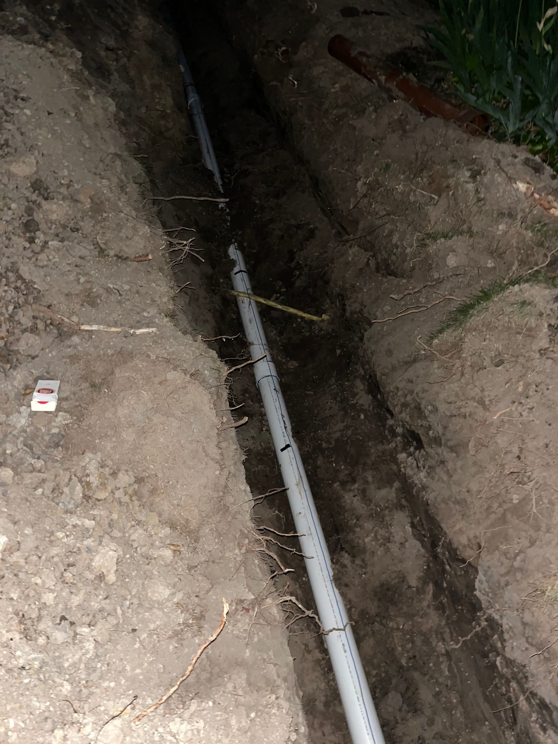 Trench in the ground with a long, white pipe running through it, presumably for utilities.