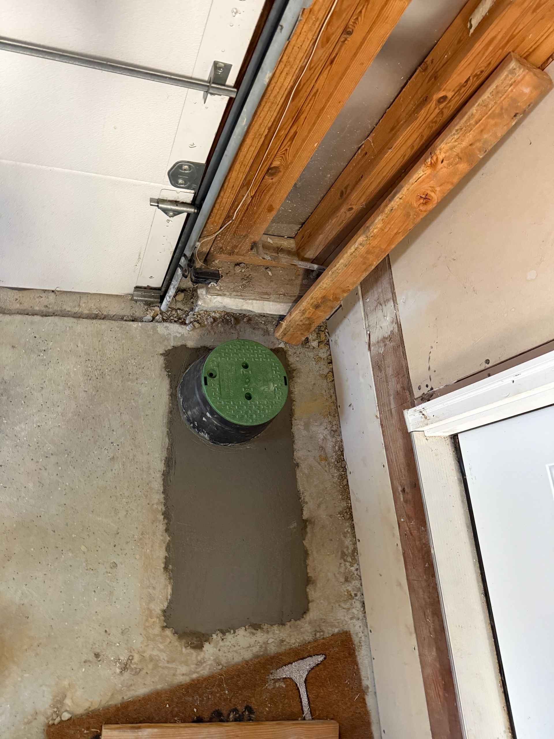 A garage interior with a concrete wall and a green-lidded cylindrical object embedded in the wall. Wooden beams and a track for the garage door are visible above.