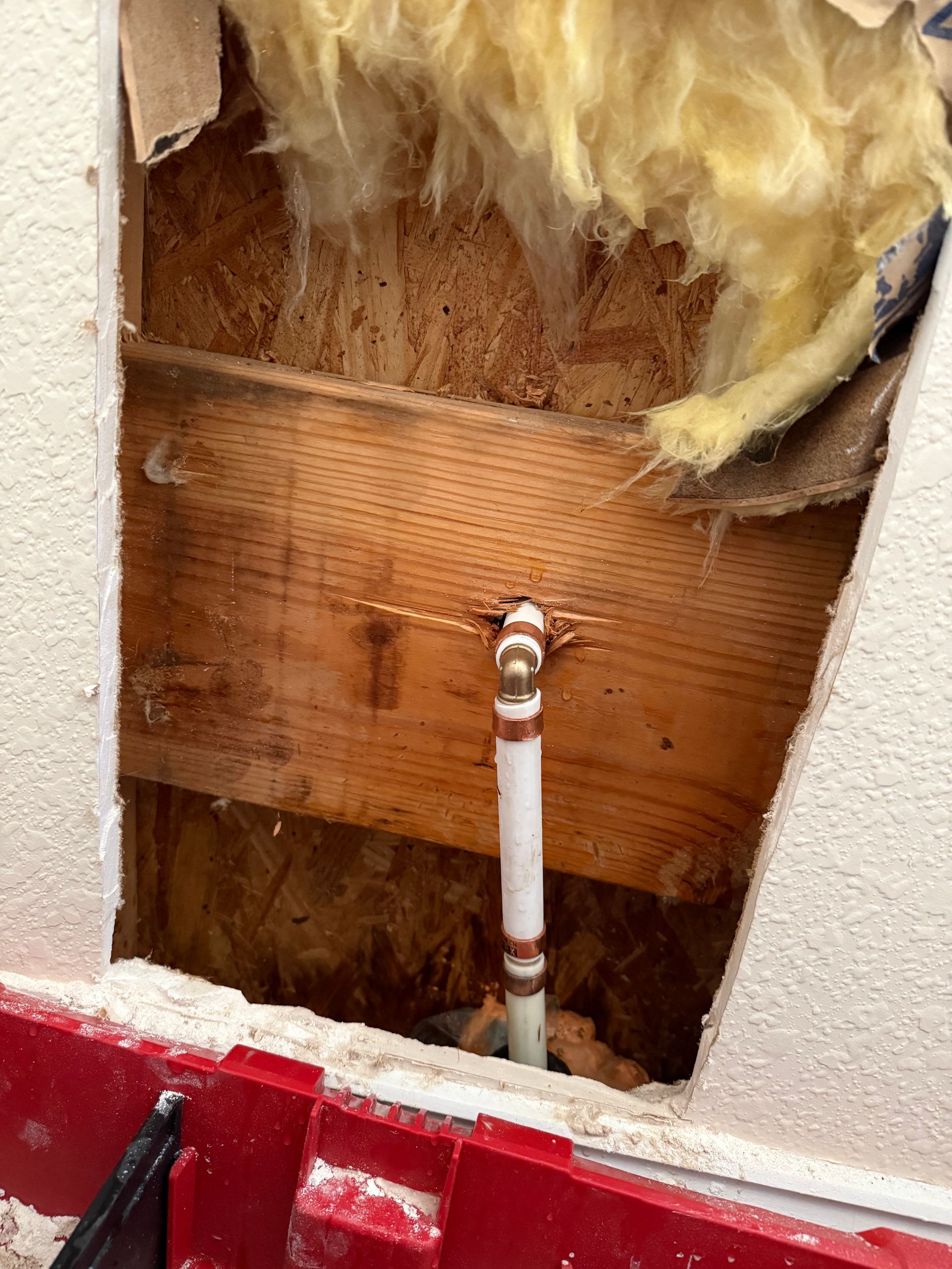 A plumbing pipe inside a wall, exposed due to a hole. Insulation and wood are visible.