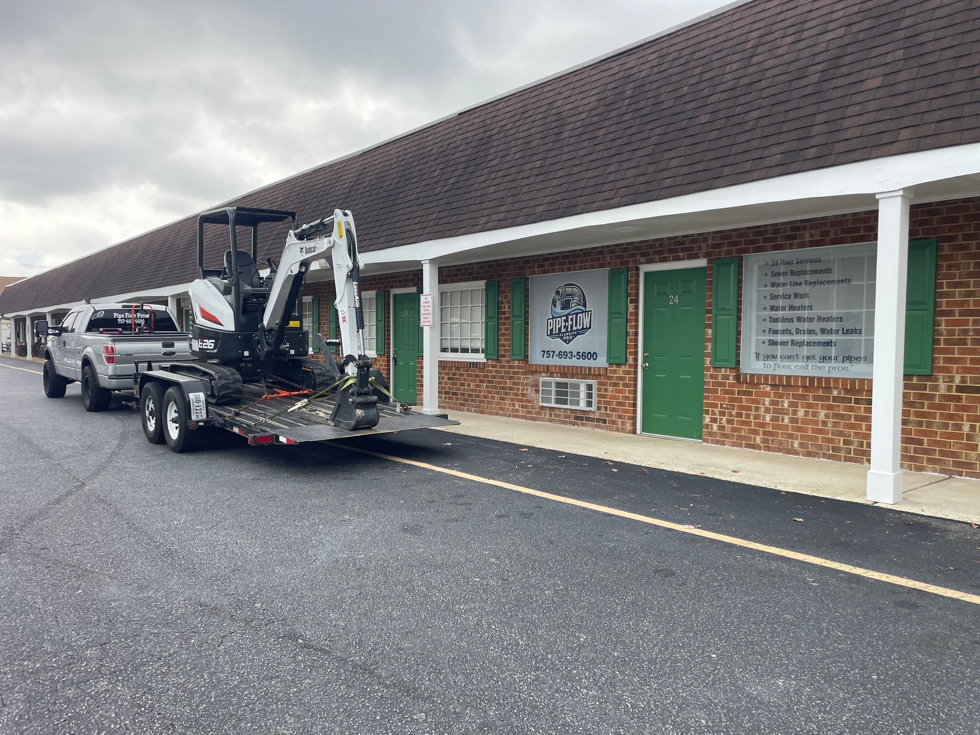 A truck and trailer with a mini excavator parked in front of a motel.