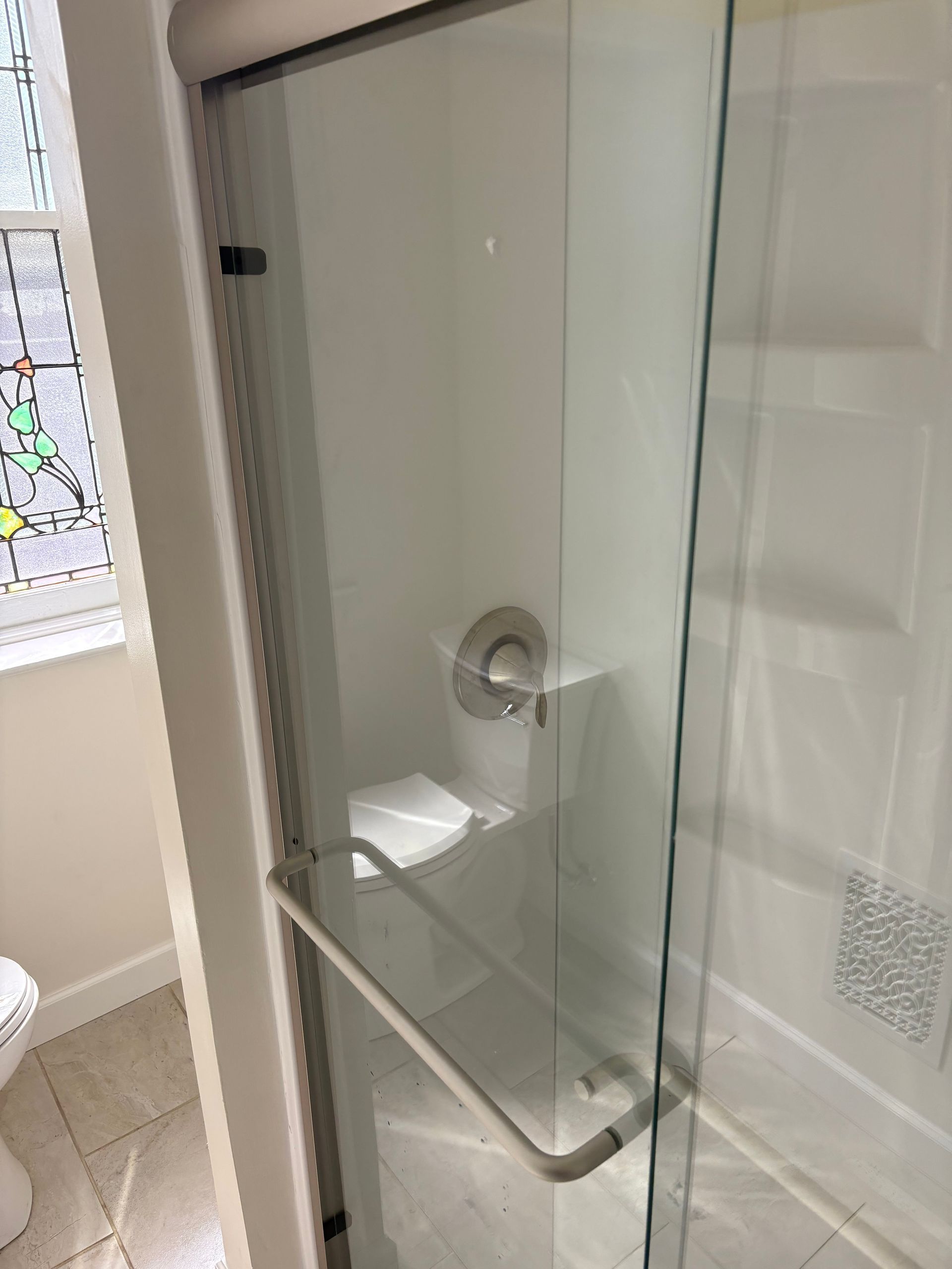 Accessible shower with grab bar and folding wooden seat; white walls, shower base, chrome fixtures.
