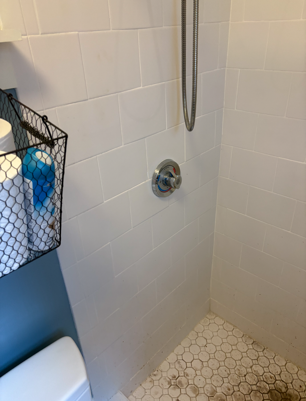 Shower with white subway tiles and small, light-colored floor tiles. A chrome shower head is visible.