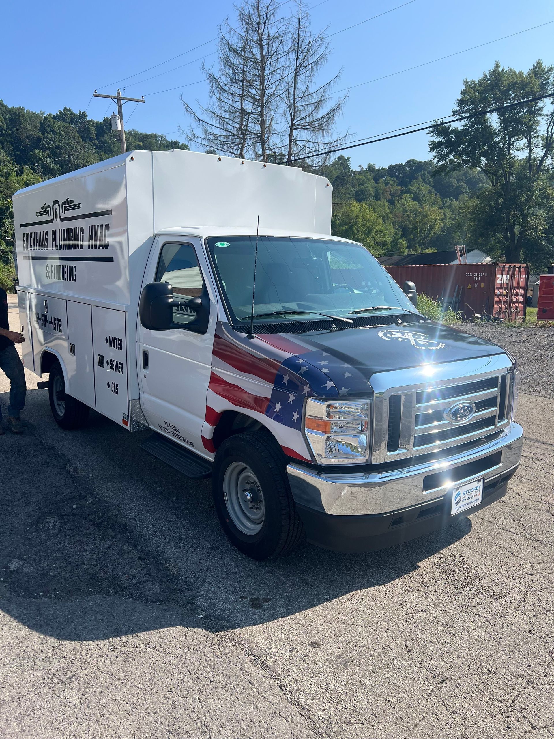 White service truck with American flag paint job parked on gravel, outdoors.