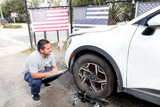 A man is kneeling down next to a white car with a flat tire.