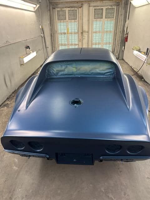 A blue car is sitting in a garage being painted.