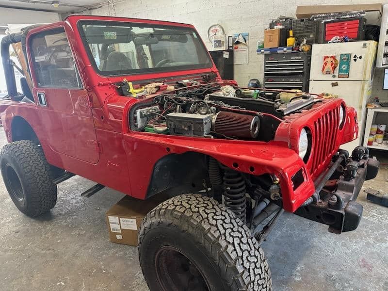 A red jeep is being worked on in a garage.