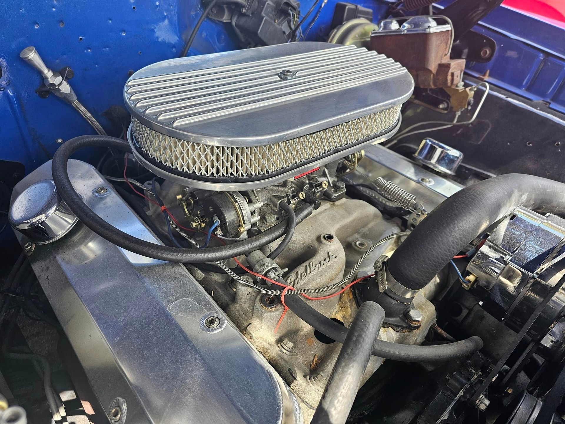 A close up of a blue car engine with a carburetor.