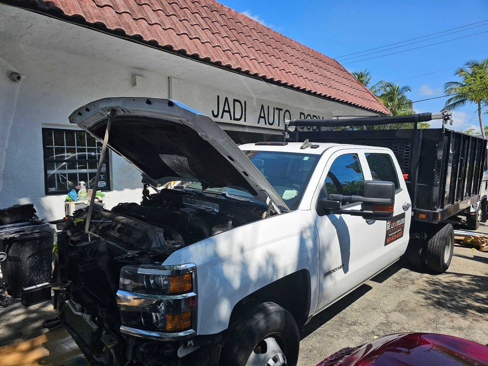 A white truck with its hood up is parked in front of a building.