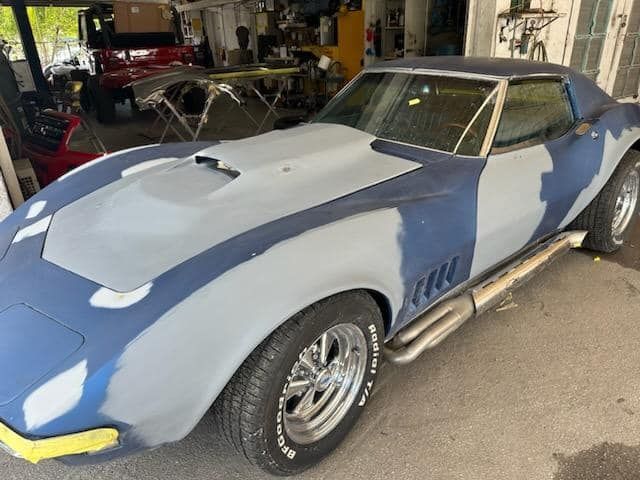 A blue and white corvette is being painted in a garage.