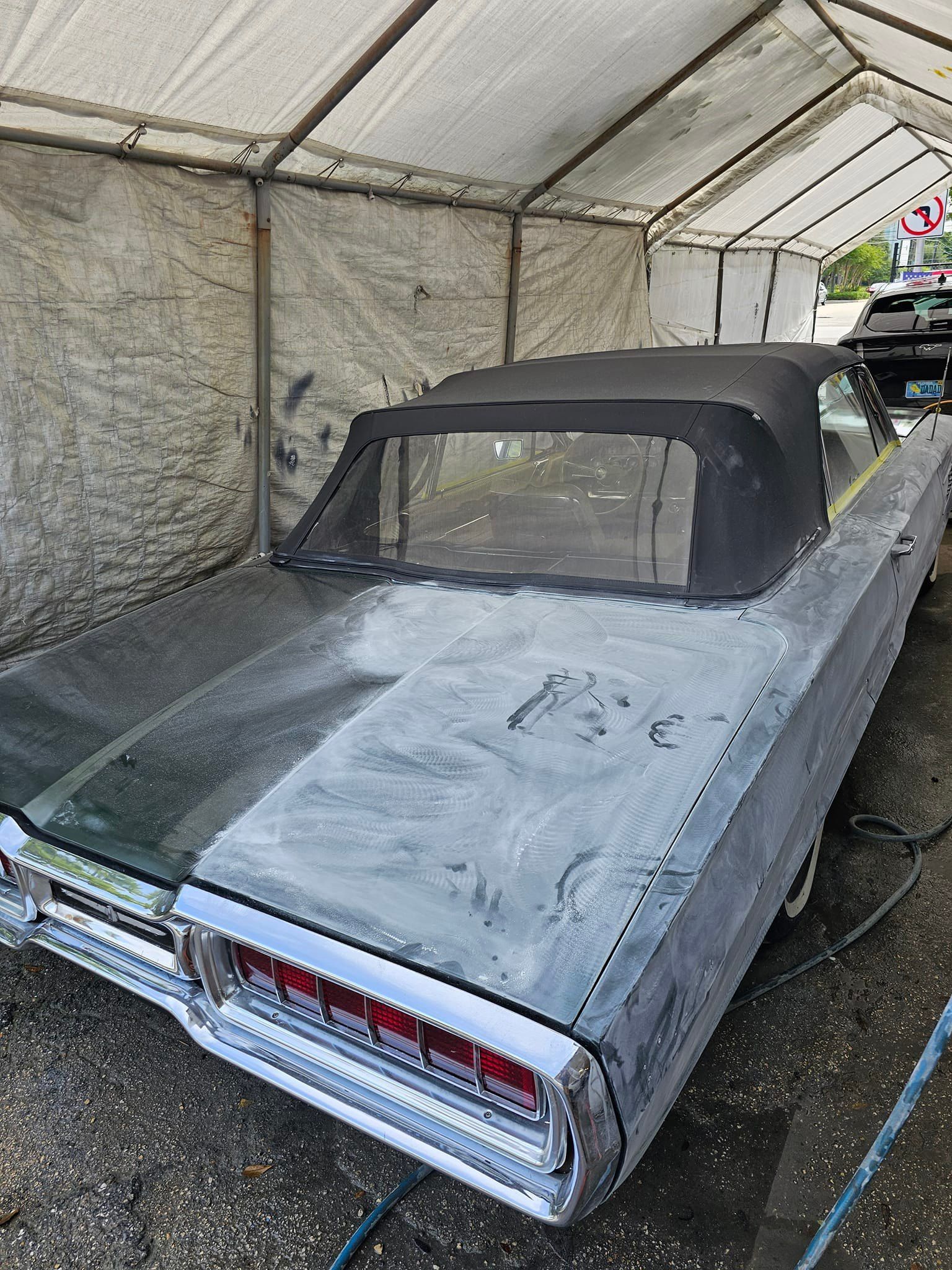 A car is sitting under a tent in a parking lot.