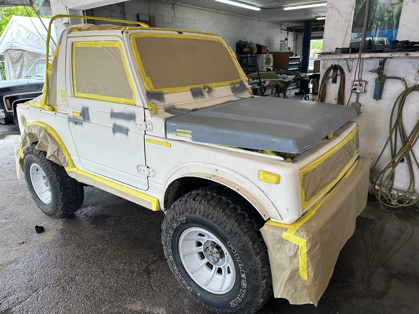 A white jeep is being painted in a garage.