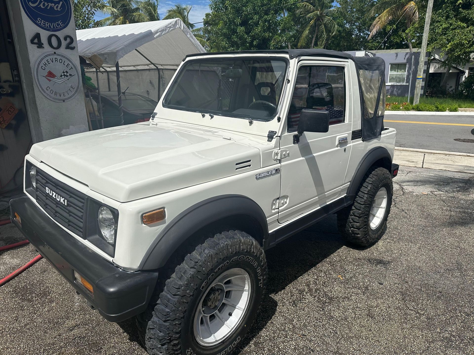 A white suzuki samurai is parked on the side of the road.