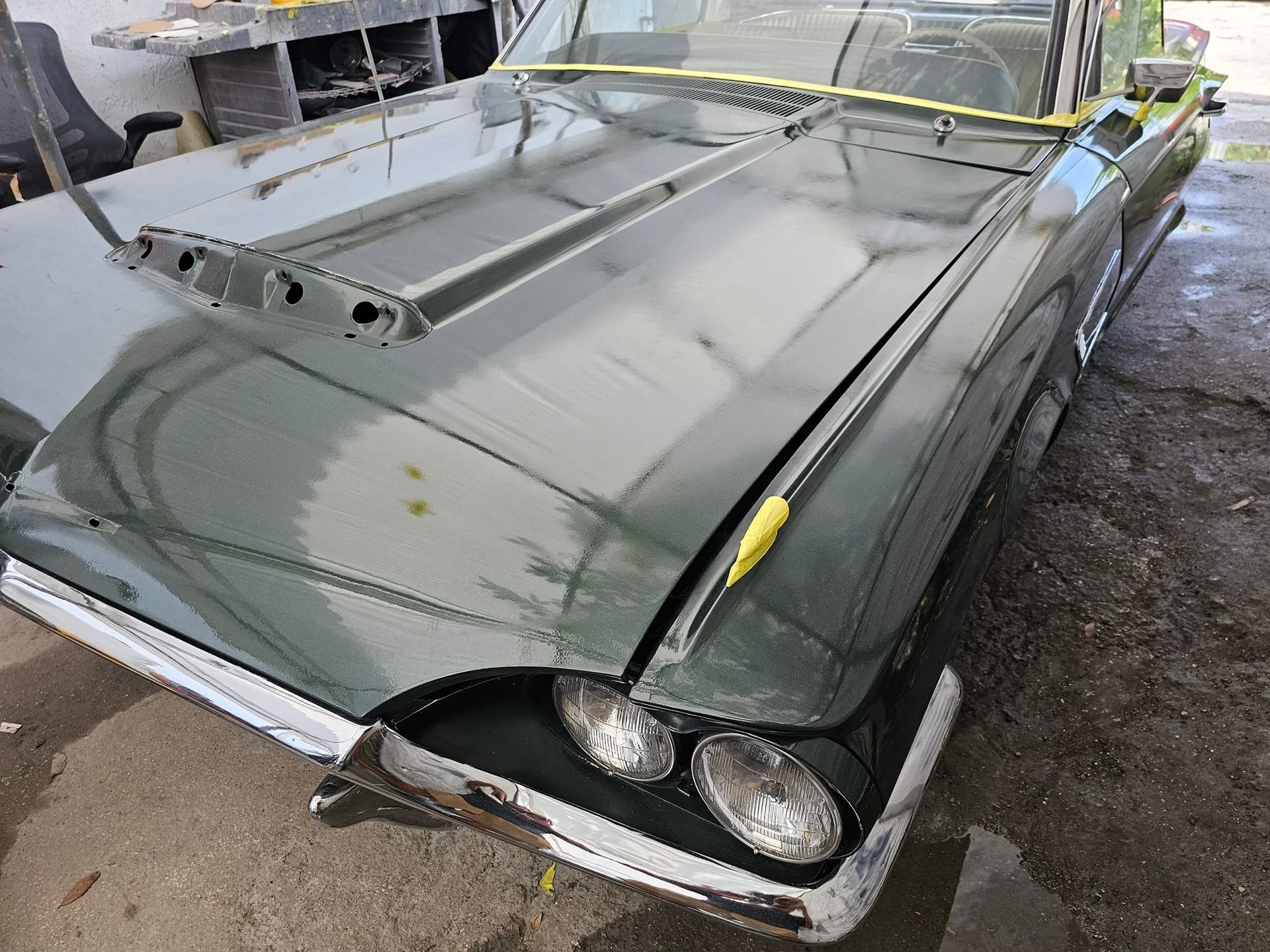 A black car with the hood up is sitting in a garage.
