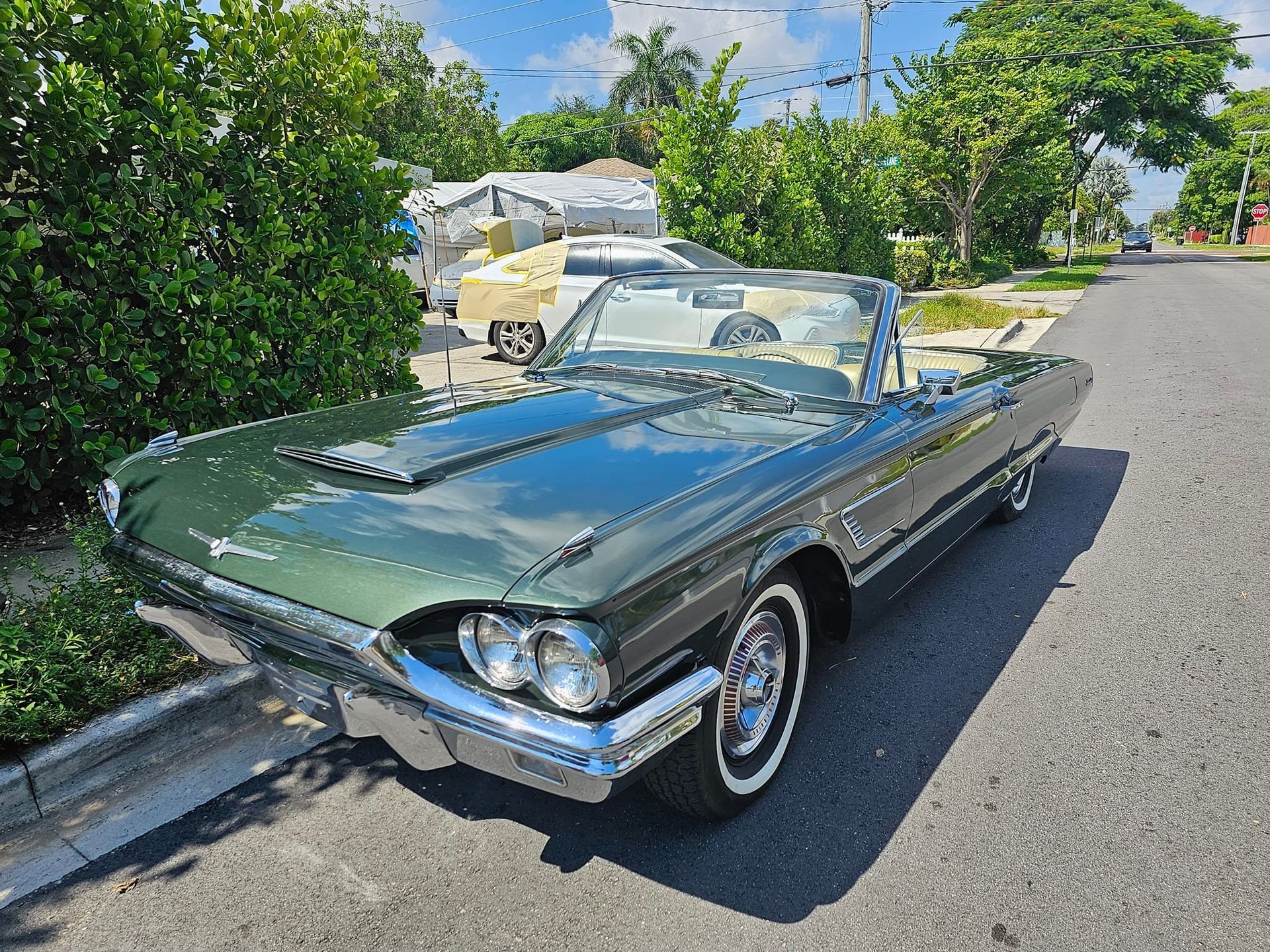 A green thunderbird convertible is parked on the side of the road.