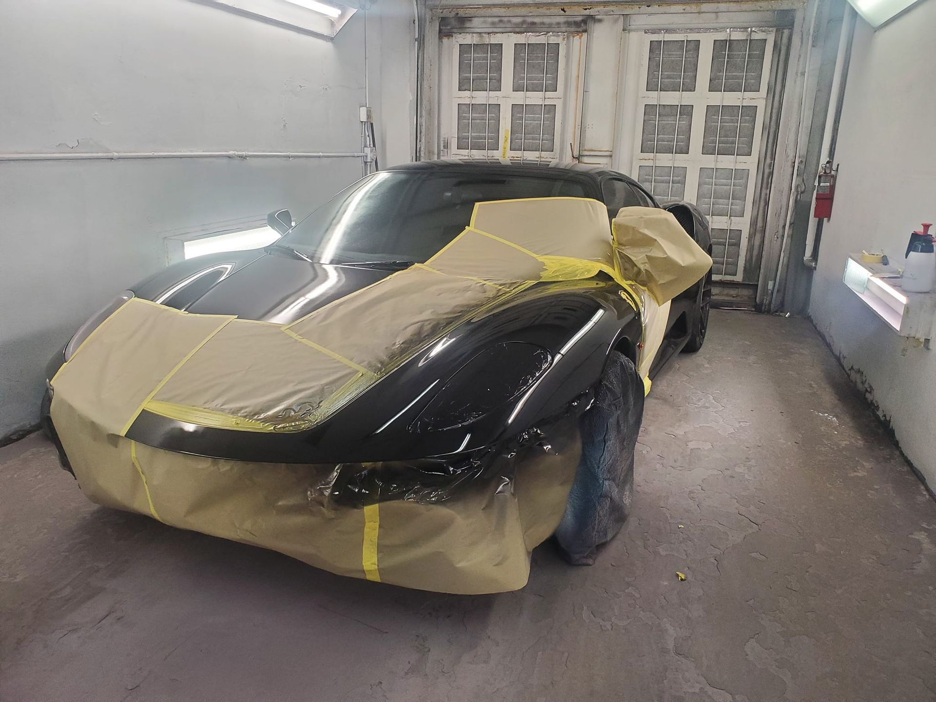 A black sports car is being painted in a garage.