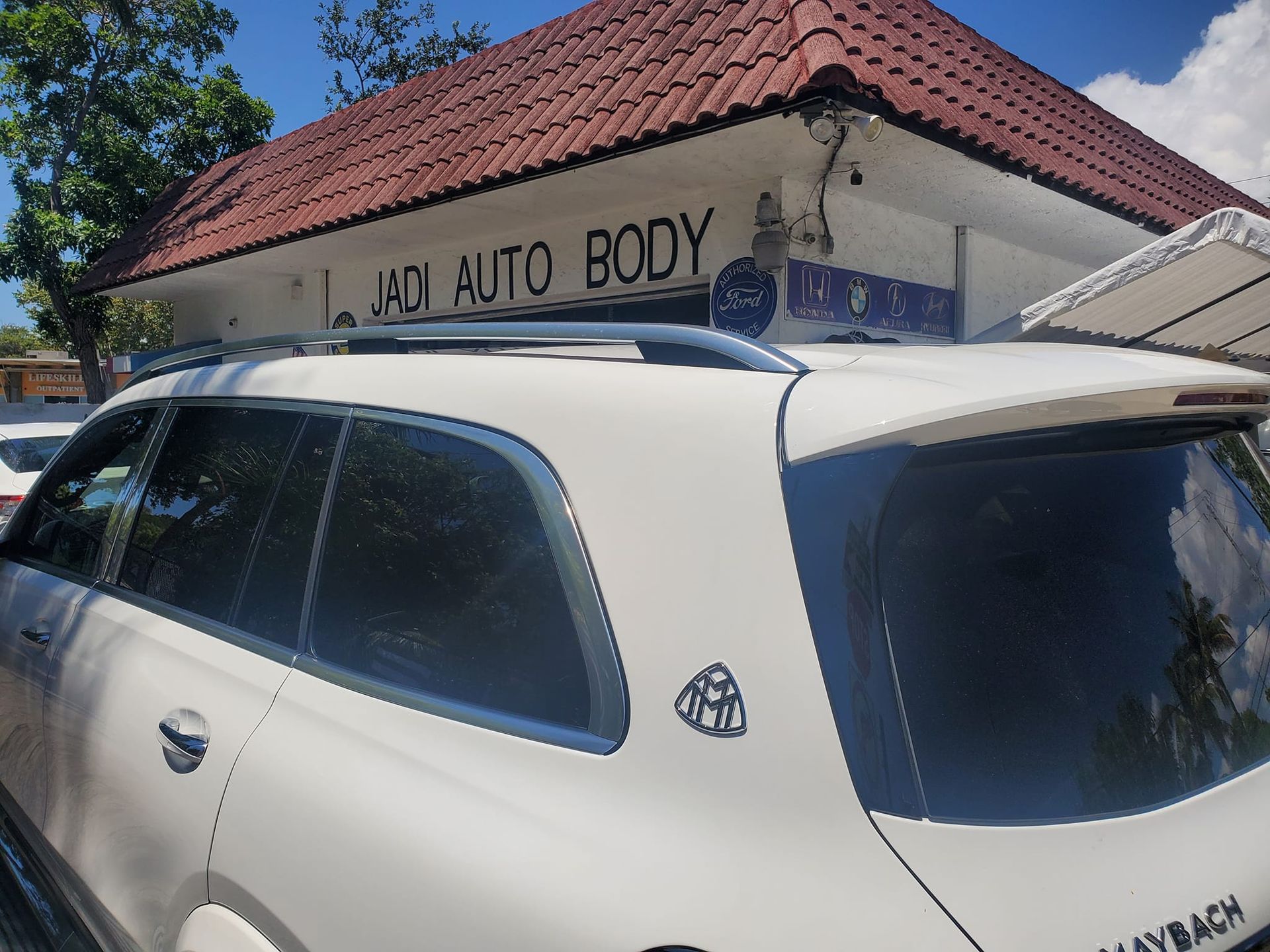 A white car is parked in front of an auto body shop