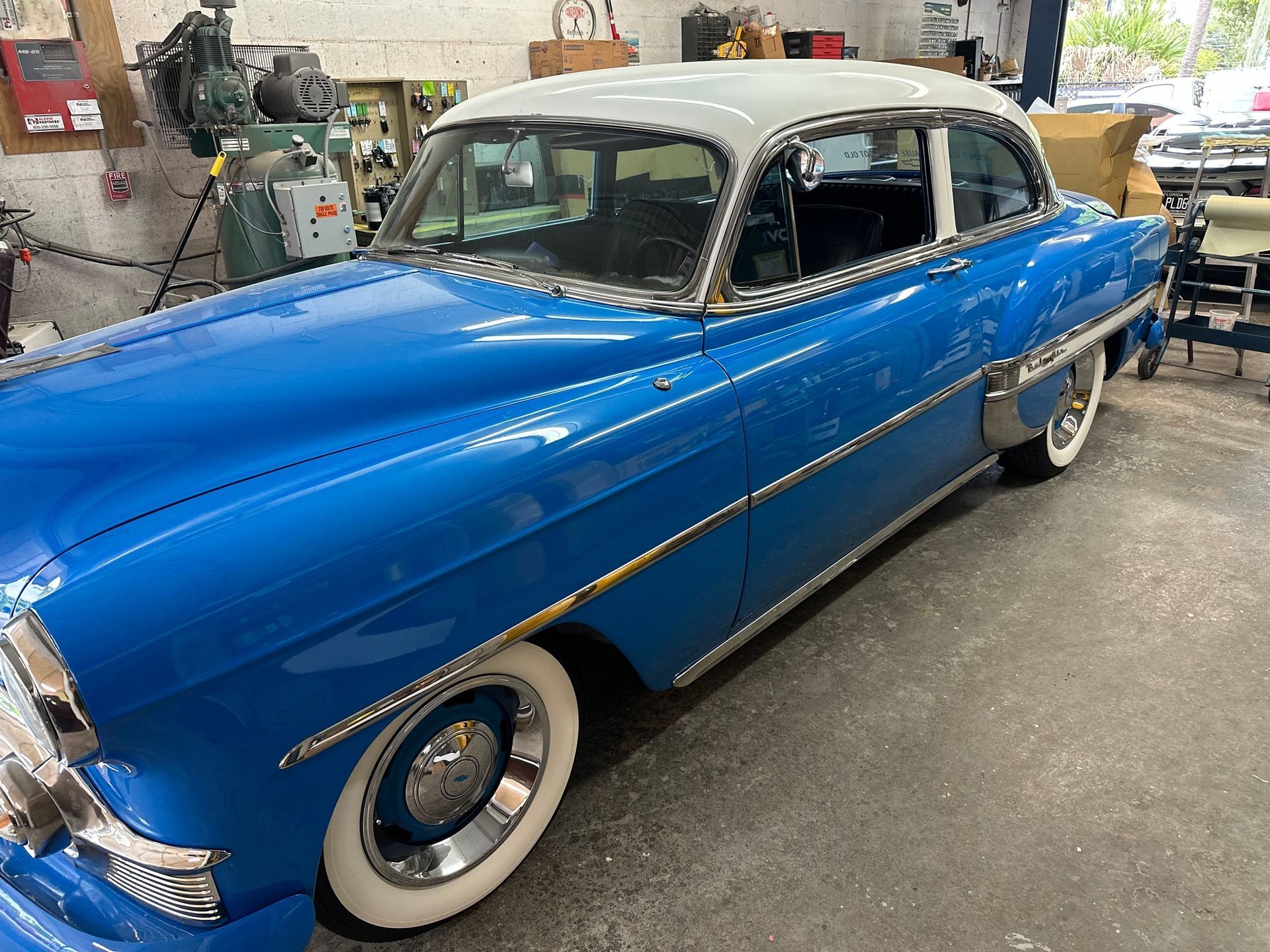A blue car with white tires is parked in a garage.