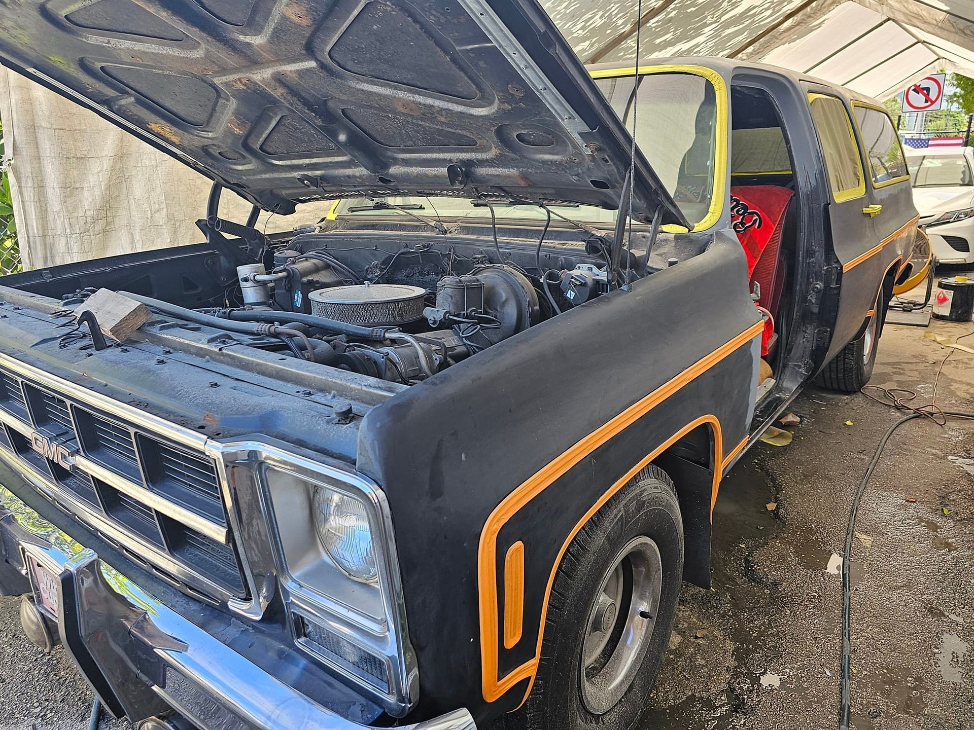 A black truck with the hood open is parked in the dirt.