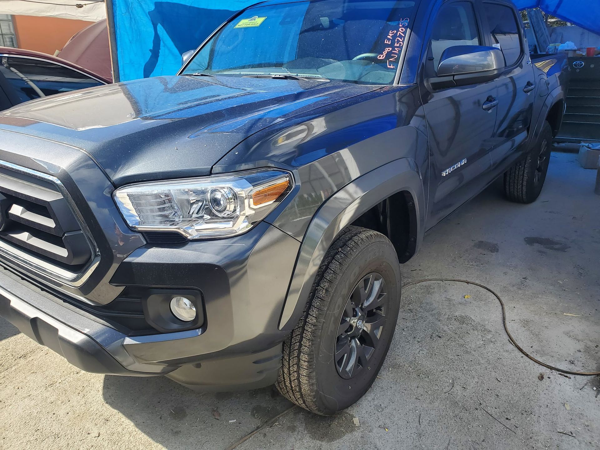 A black toyota tacoma truck is parked in front of a blue tarp.