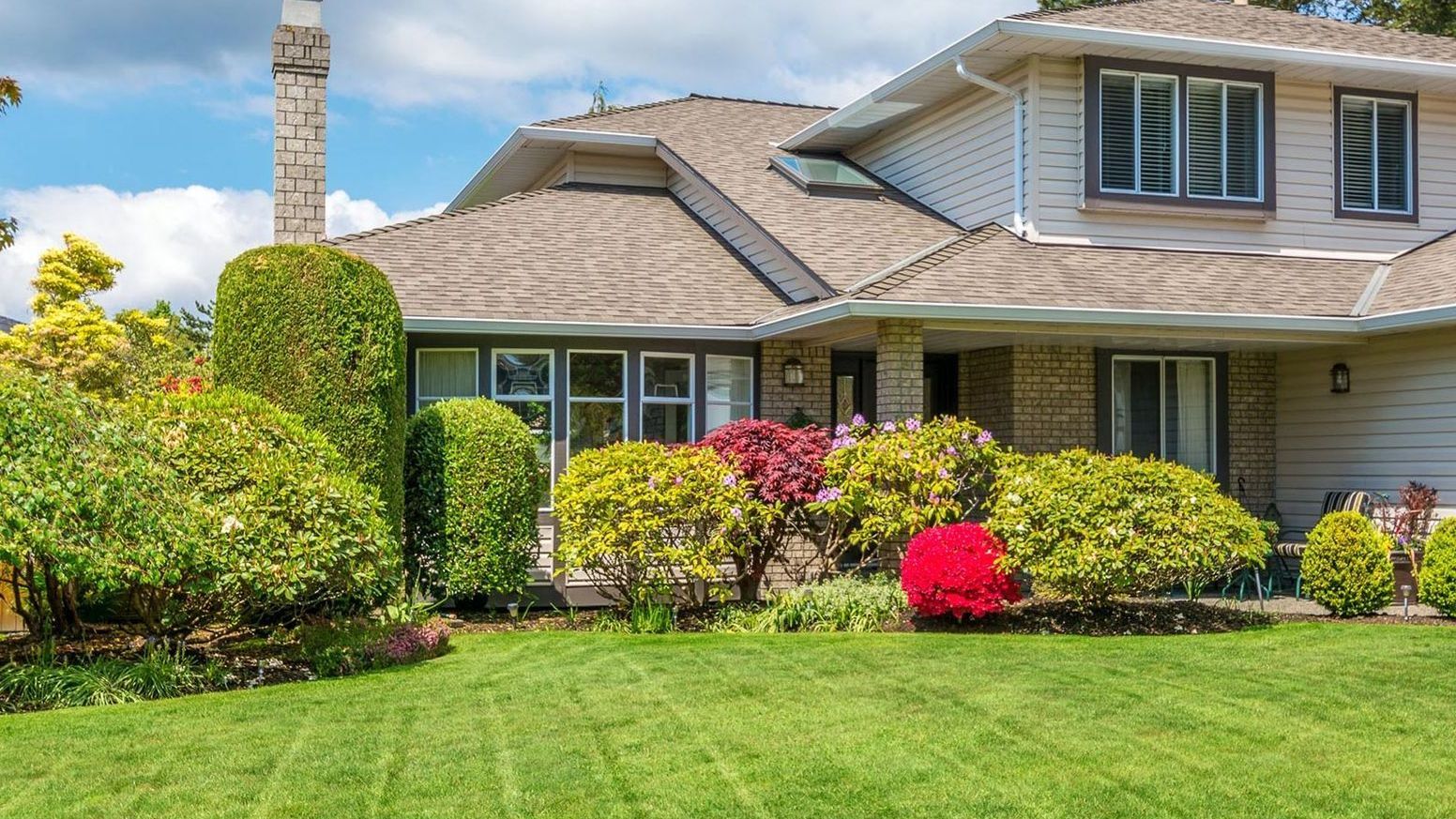 A large house with a lush green lawn and bushes in front of it.