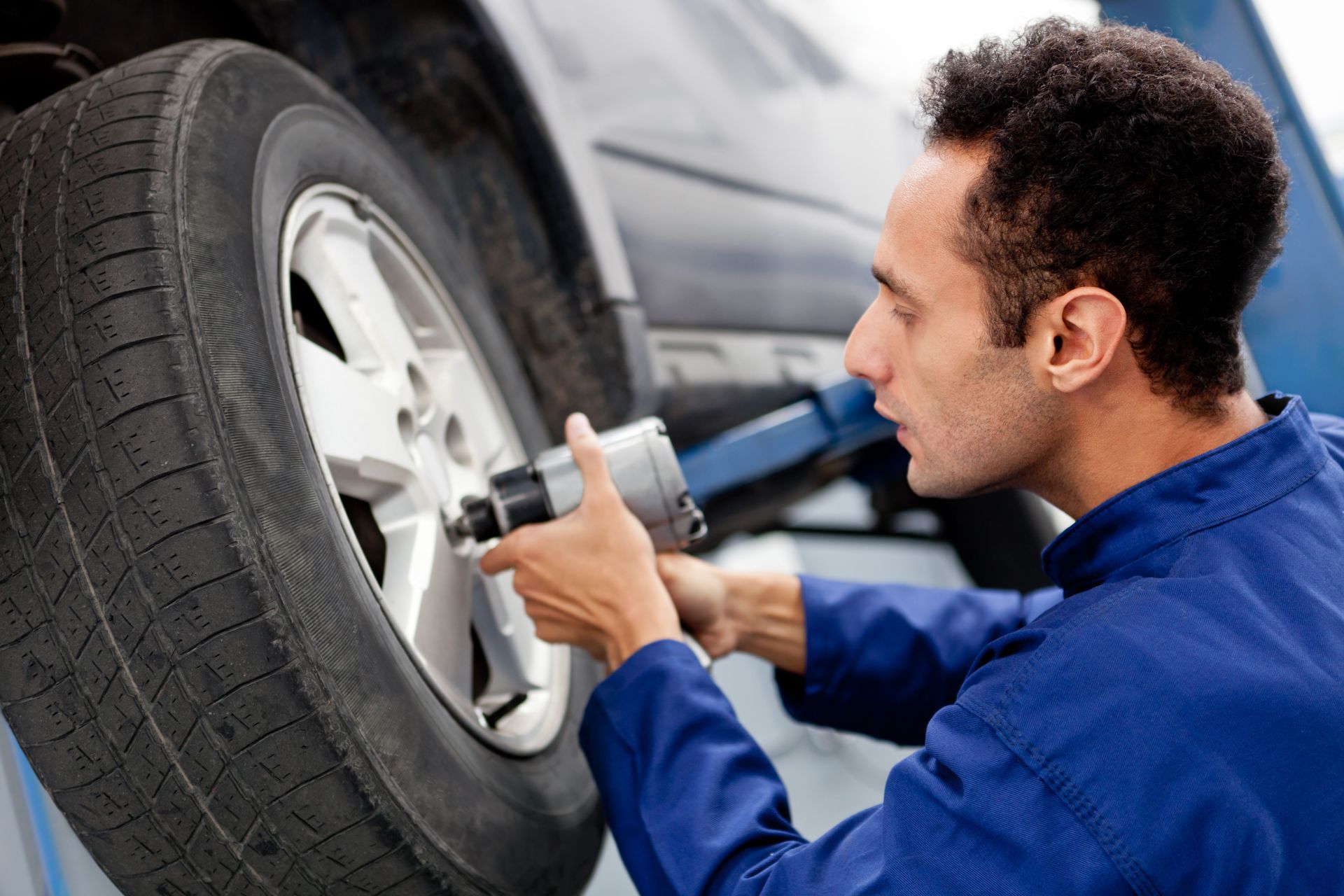 Mechanic in blue coveralls checking a car tire with a tool in a garage