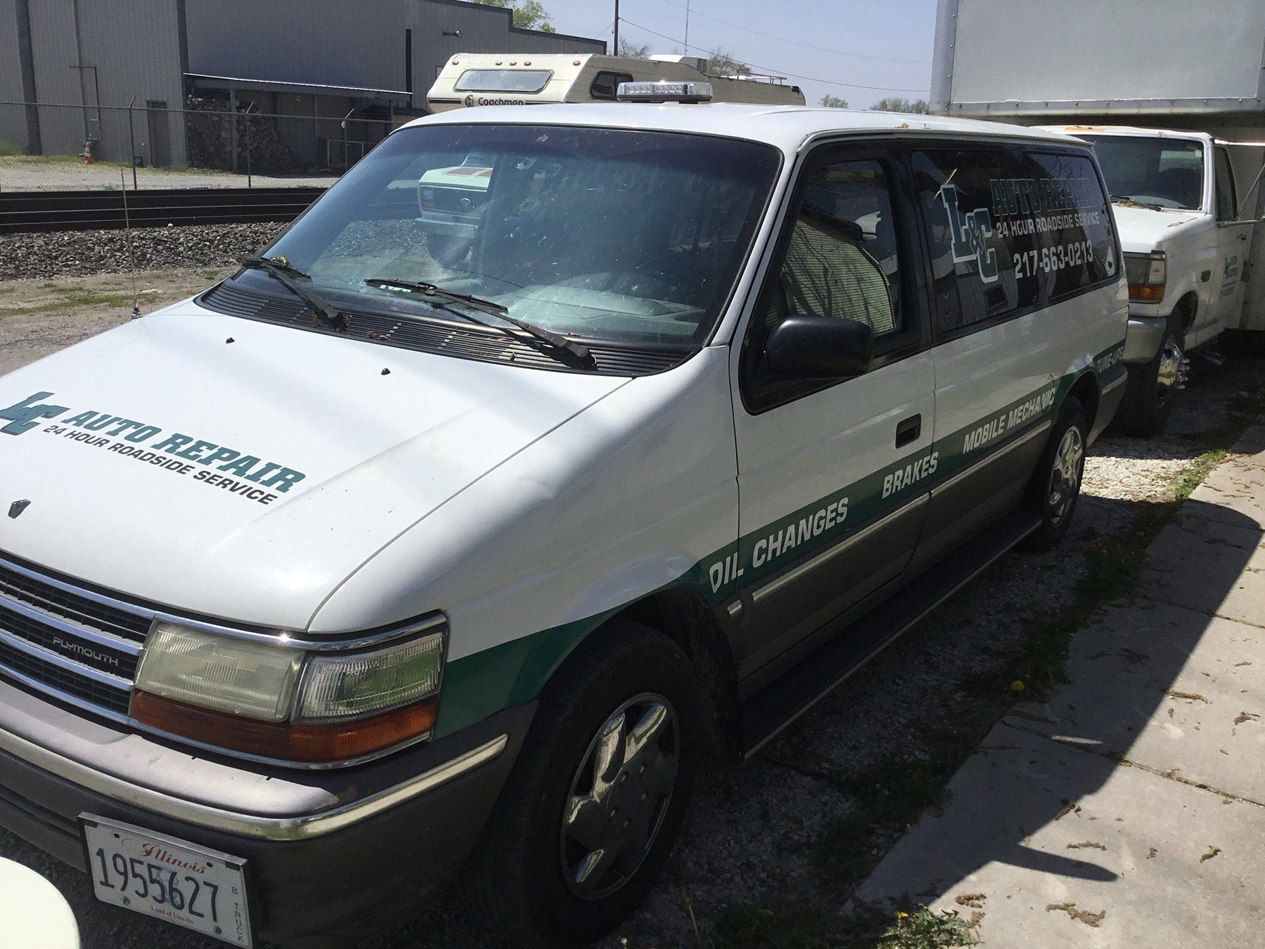 White and green minivan parked beside a white trailer on a sunny street