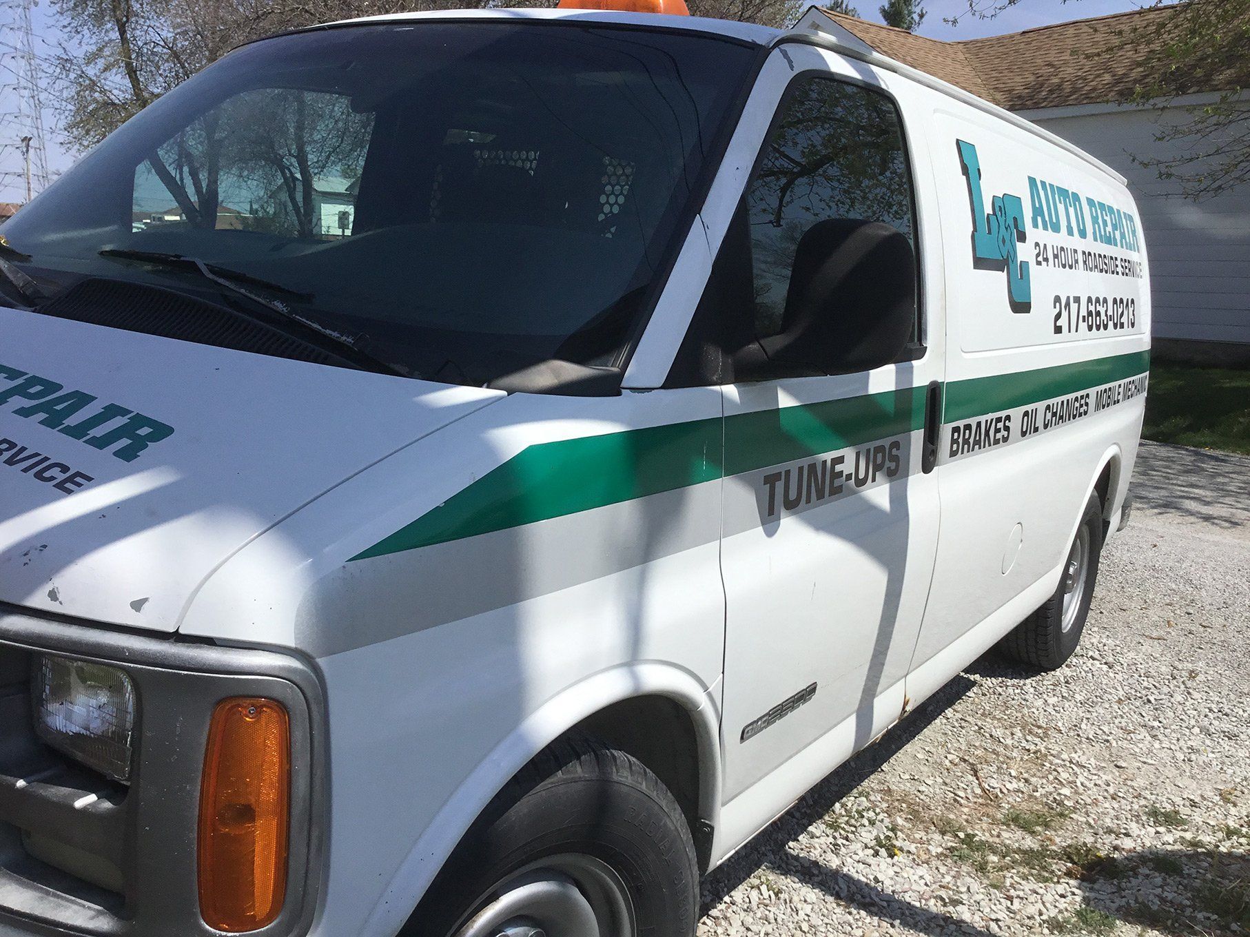 White utility van with green stripe parked on gravel near a building, side logo visible