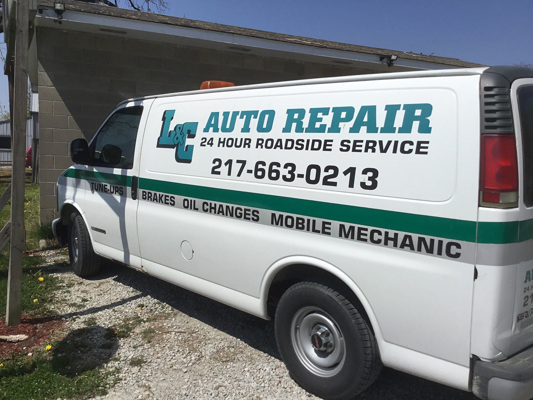 White auto repair van with “24 hour roadside service” text parked beside a building and garage door