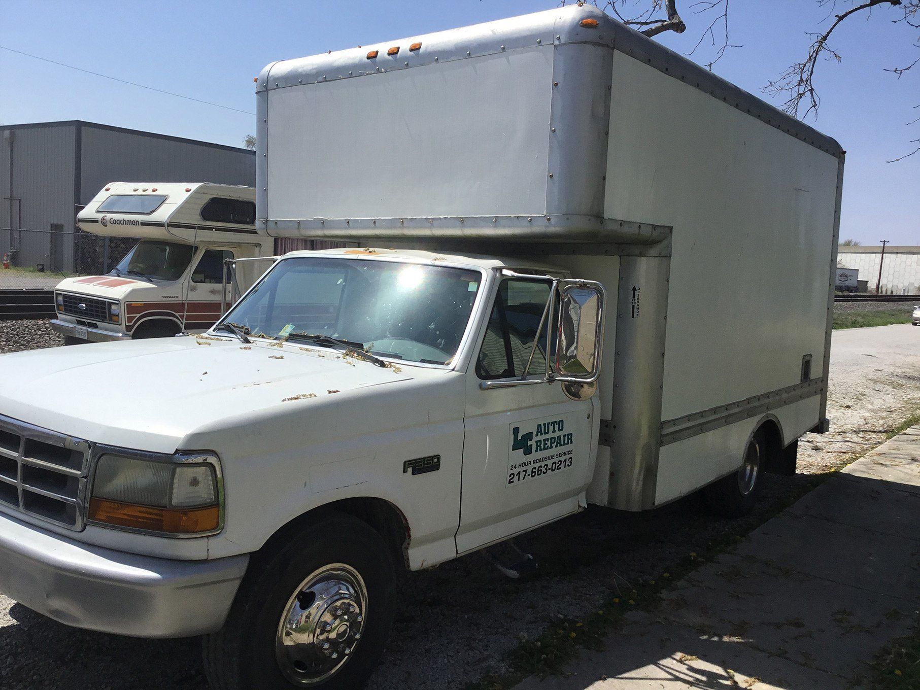 White box truck parked outdoors in an industrial lot, viewed from the front-left side.