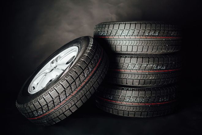 Stacked black car tires with one leaning wheel rim on a dark background