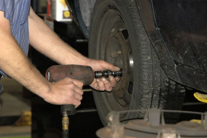 Mechanic using a pneumatic impact wrench to remove a car wheel lug nut