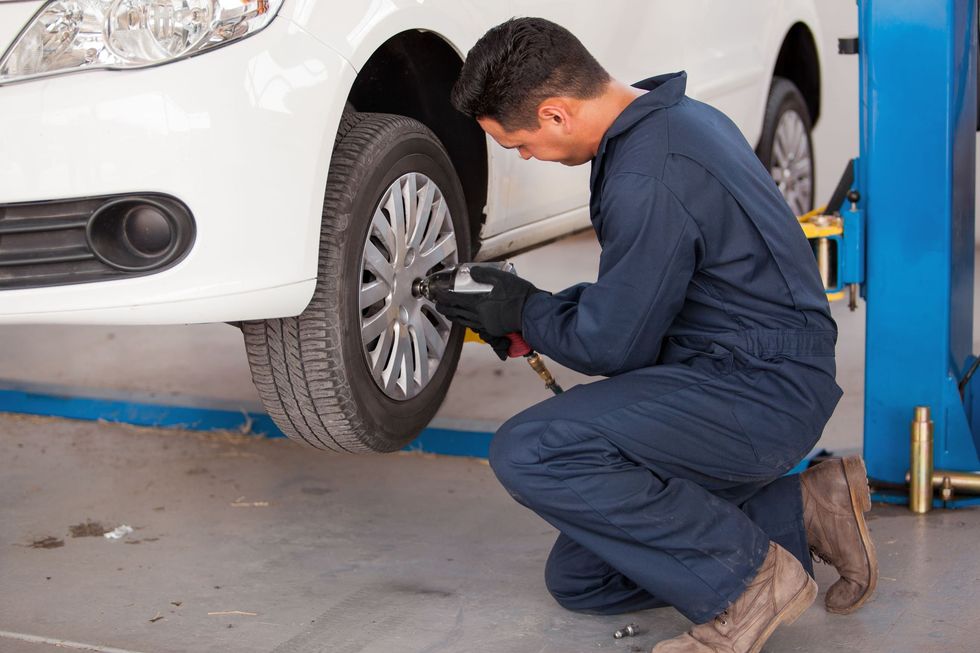 Mechanic tightening a car’s front wheel in a garage with a hydraulic lift