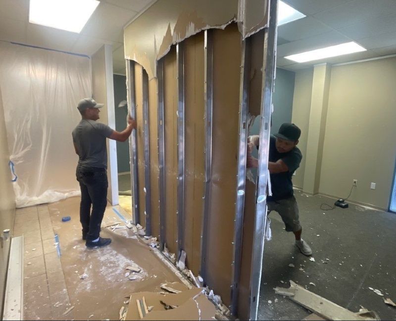Two men are working on a wall in a room