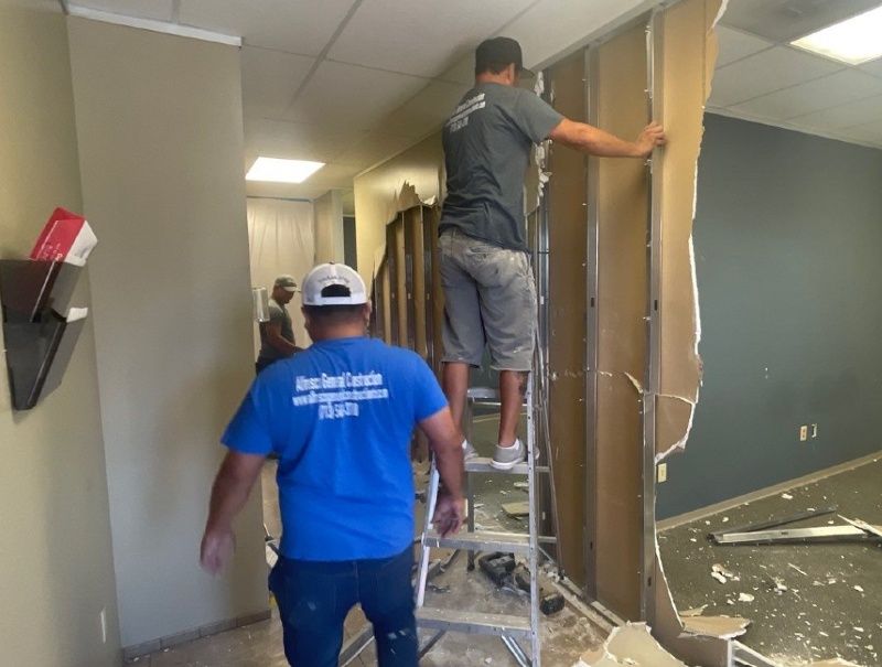 Two men are working on a wall in an office building.