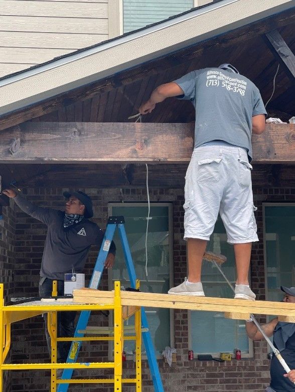 Two men are standing on a scaffolding working on a roof of a house.