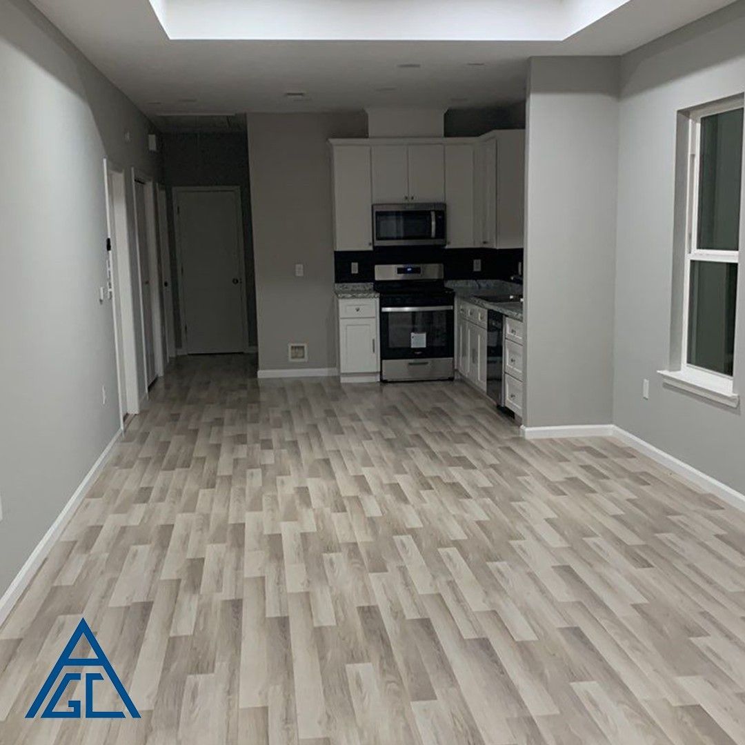 A living room with hardwood floors and a kitchen in the background.