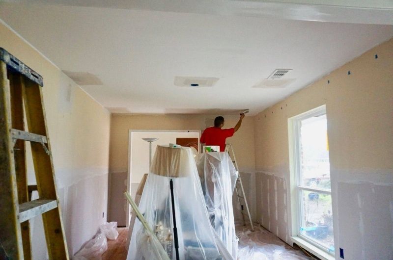 A man is standing on a ladder painting the ceiling of a room.