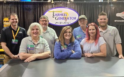 A group of people are posing for a picture in front of a Tarheel Generator sign.