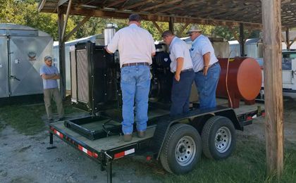 Three men are standing on a trailer looking at the generator.