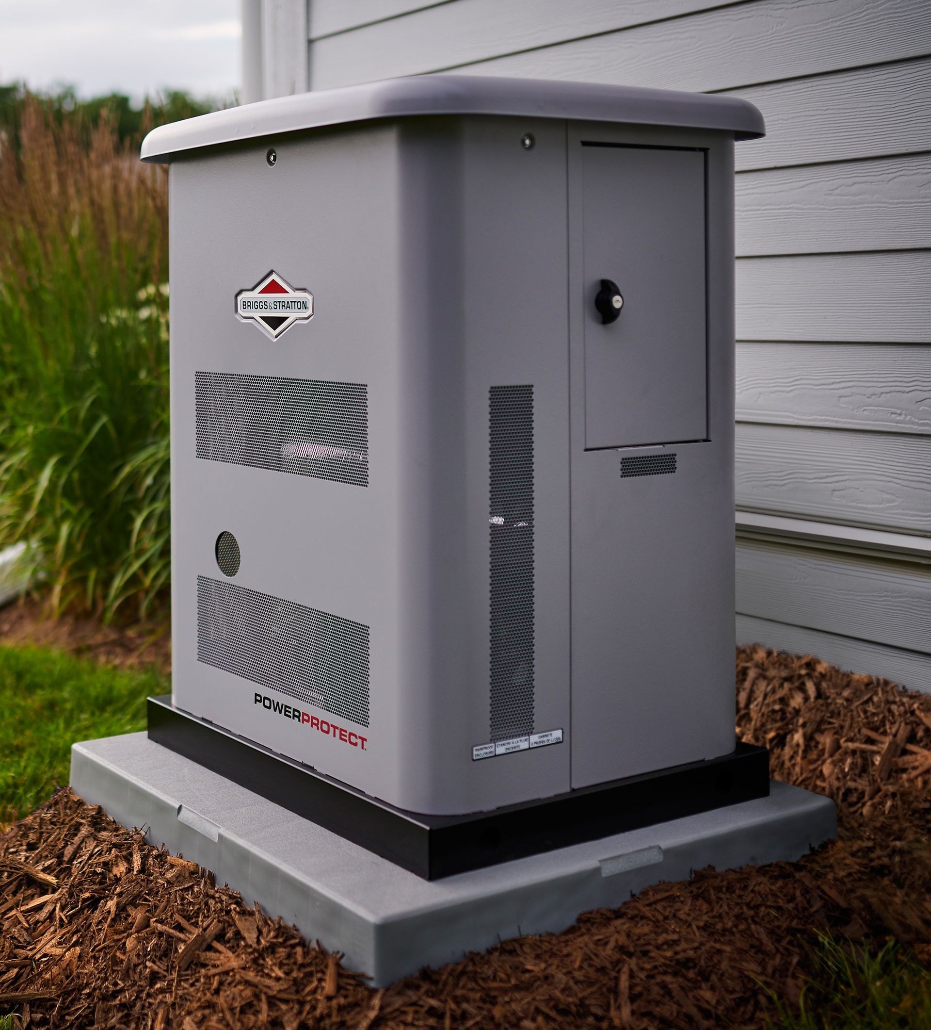 A generator is sitting on a concrete base in front of a house.