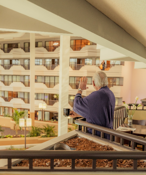 Person in a purple sweater looking over a balcony at a bright indoor atrium with multiple floors.