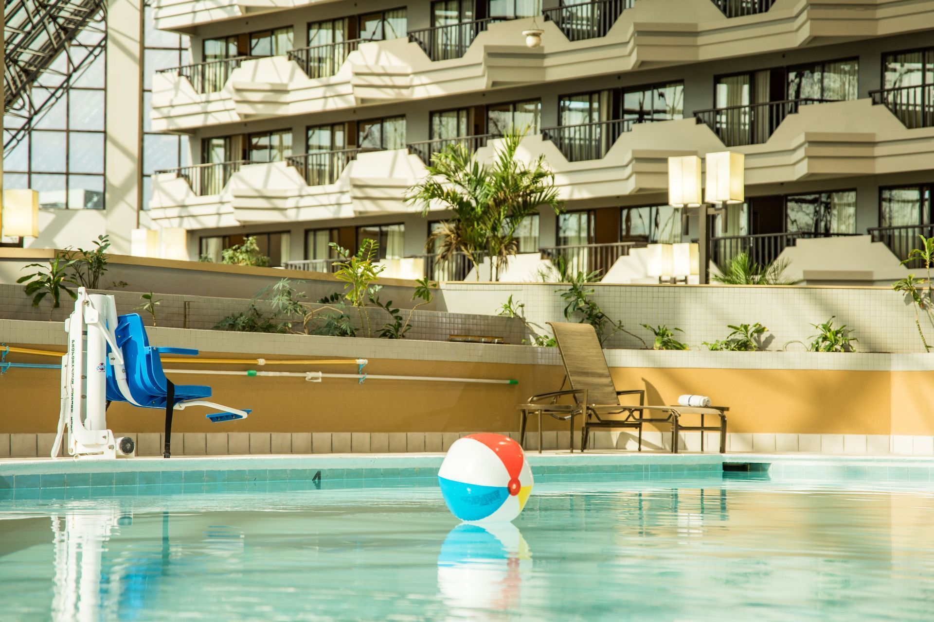 Indoor hotel pool with a blue-and-red beach ball and a blue lounge chair by the water
