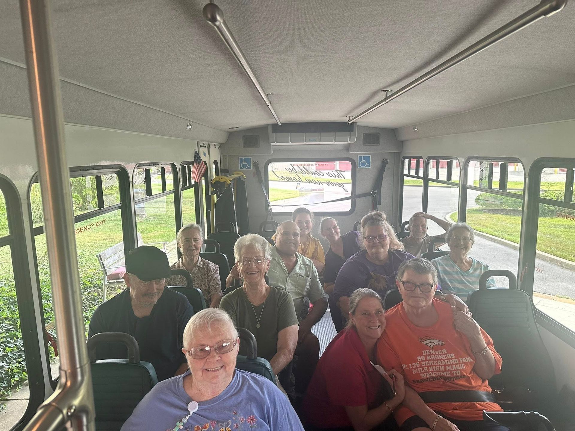 Passengers seated on a shuttle bus, facing the camera and smiling.