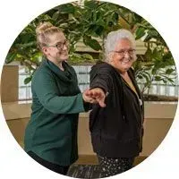 Two smiling people in green and black tops point together in a plant-filled indoor space.
