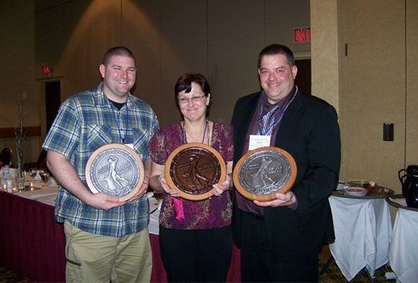 Three people are standing next to each other holding plaques.