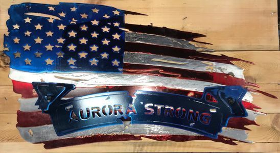 A metal american flag with the words `` aurora strong '' written on it is sitting on a wooden table.