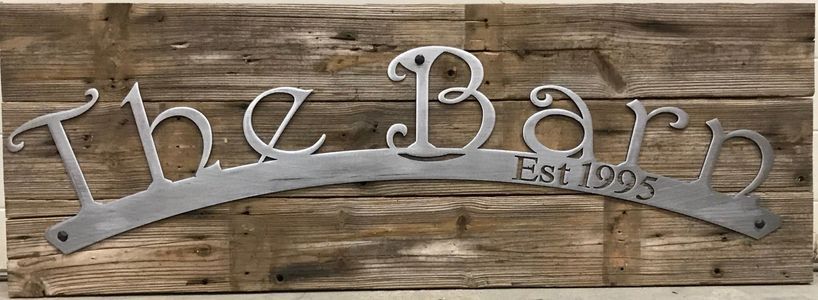 A metal sign on a wooden wall that says `` the barn ''.