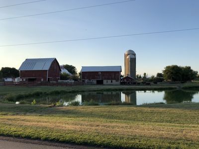 A farm with two barns and a silo next to a pond.