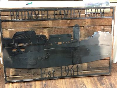 A metal sign with a barn and silo on it is sitting on a wooden table.